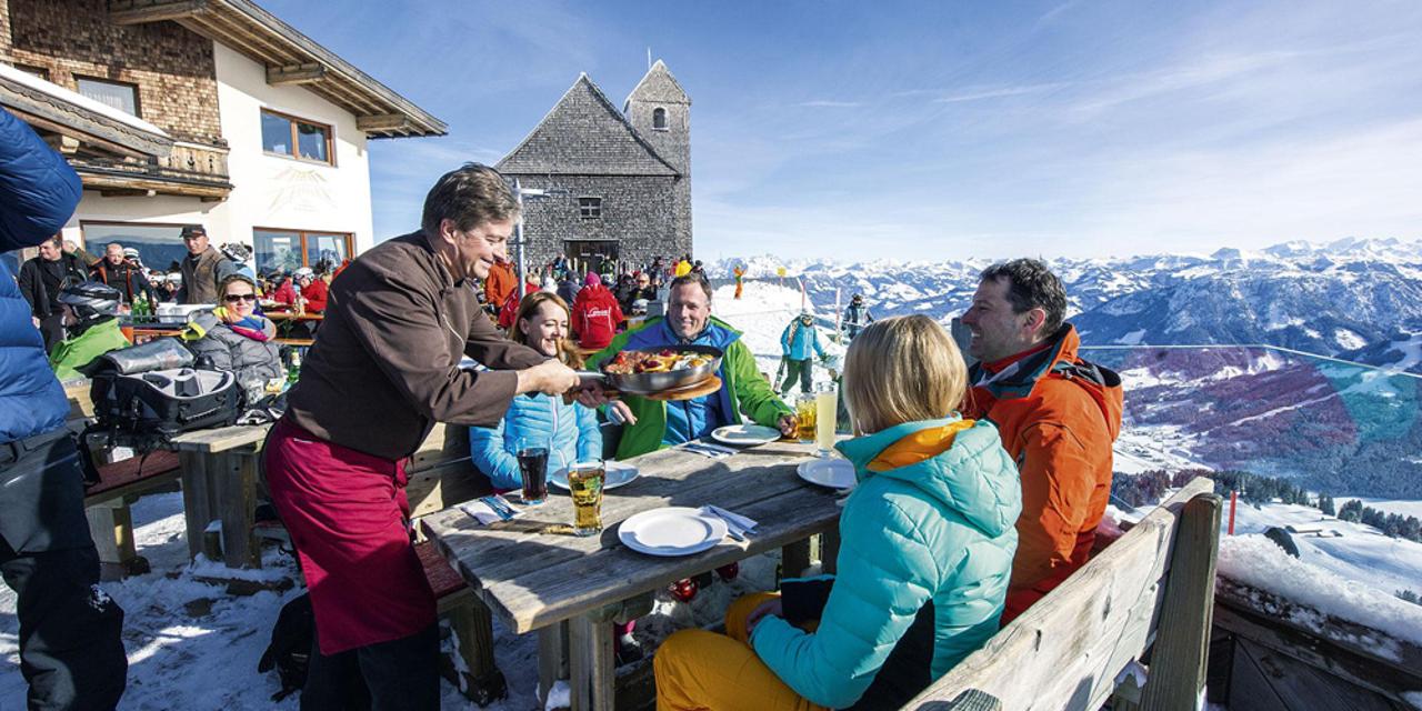 Skifahrer beim Kaiserschmarrn-Essen auf einer Skihütte in der SkiWelt Wilder Kaiser