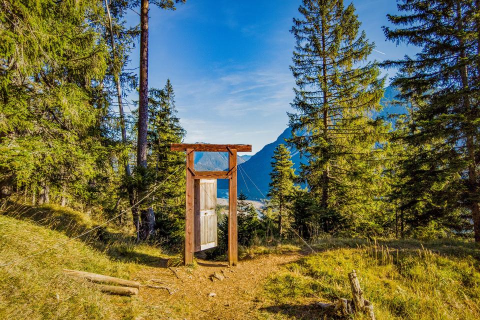 Sonniger Blick mit blauem Himmer auf den Baichlstein durch eine am Wegrand stehende Holztür Porta Alpina