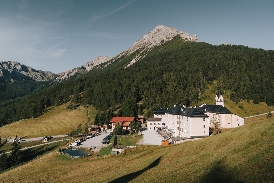 Berge, Wald, Bäume, Wiese, Wahlfahrtskloster, Autos stehen am Parkplatz, Straße, Kloster & Natur Resort Maria Waldrast am Fuß der Serles im Sommer