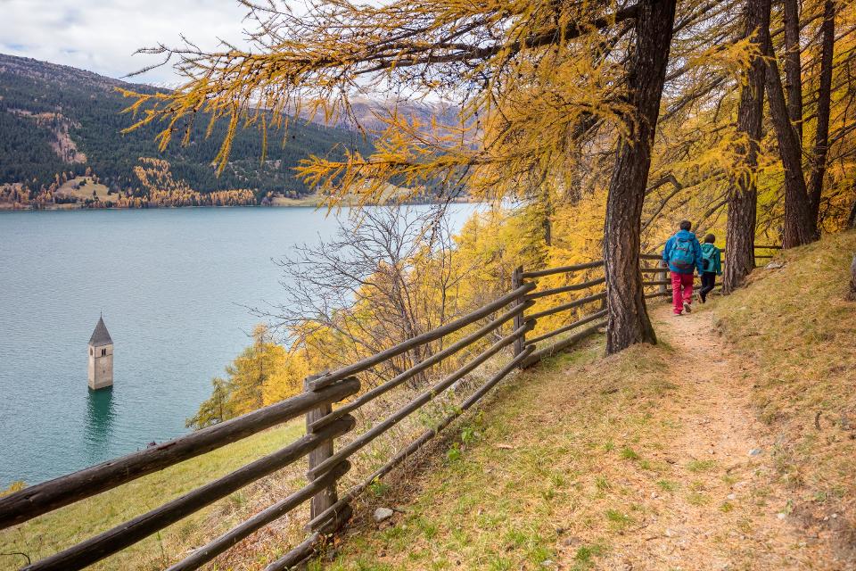 Wandern auf dem Vinschger Hoehenweg mit Blick auf den Kirchturm im See von Alt-Graun